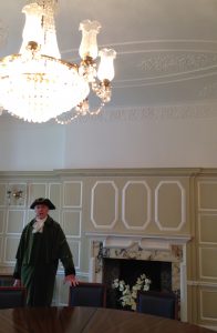 Gentleman in tricorn hat and green coat, in spacious, cream panelled room